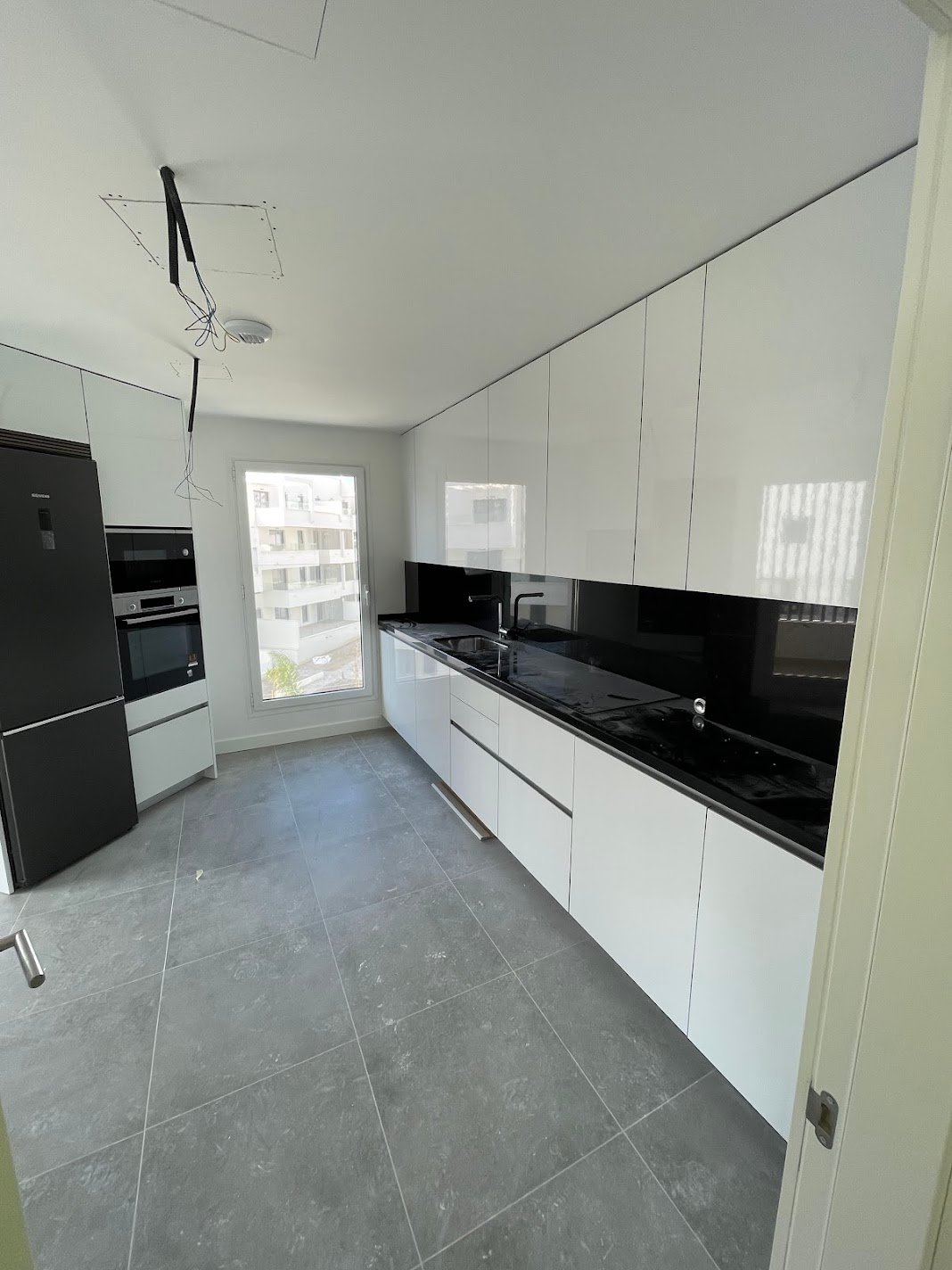 Reforma de cocina moderna blanca con encimera negra y suelo gris en Marbella - PintaReformas